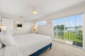 A bedroom with a large bed, a ceiling fan, a window with a view of greenery, and a sliding glass door to an outdoor area.