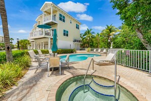 A pool area with lounge chairs, a hot tub, and a two-story building with balconies.