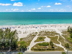 Ein Strand mit Sonnenschirmen und Menschen. Eine Straße mit einer Brücke und etwas Vegetation.