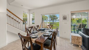 Uma área de refeições com uma mesa de madeira posta para quatro pessoas, uma escadaria e vista para uma varanda com mobiliário exterior.