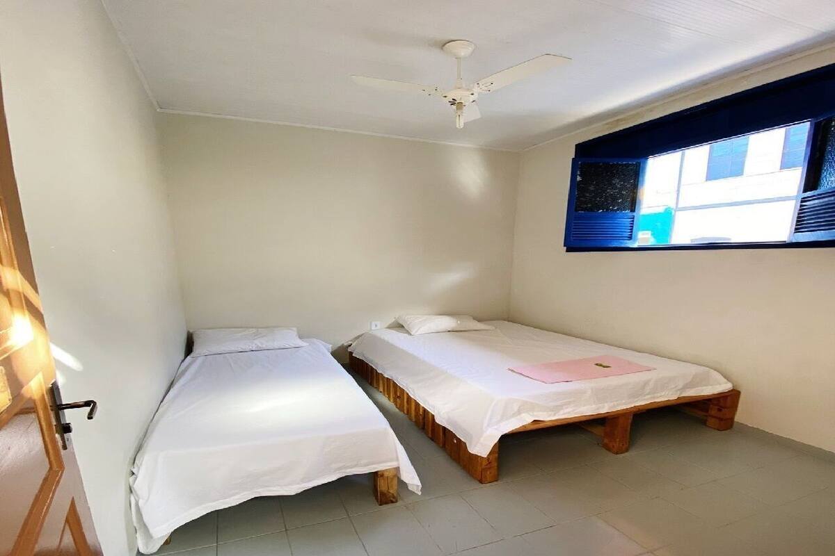 A small, clean room with two single beds, a ceiling fan, and a window with blinds.