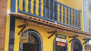 A yellow building with a blue balcony and two arched windows. - Pousada do Beco (Caravelas)