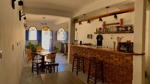 A cozy bar area with a brick counter, wooden stools, and a dining table with chairs. There are shelves with bottles and a small plant on the counter. - Pousada do Beco (Caravelas)