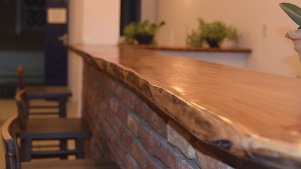 A wooden counter with a brick wall behind it, a chair, and a shelf with plants. - Pousada do Beco (Caravelas)