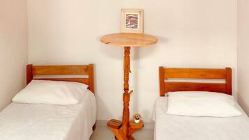 A small room with two wooden beds, a round wooden table with a picture frame, and a small plant on the floor.