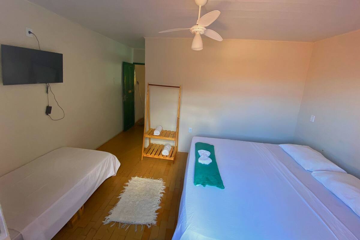 A room with two single beds, a ceiling fan, a mounted TV, and a wooden shelf with towels.