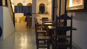 A restaurant interior with wooden tables and chairs, a staircase, and a wall with a clock and decorative lights. - Pousada do Beco (Caravelas)