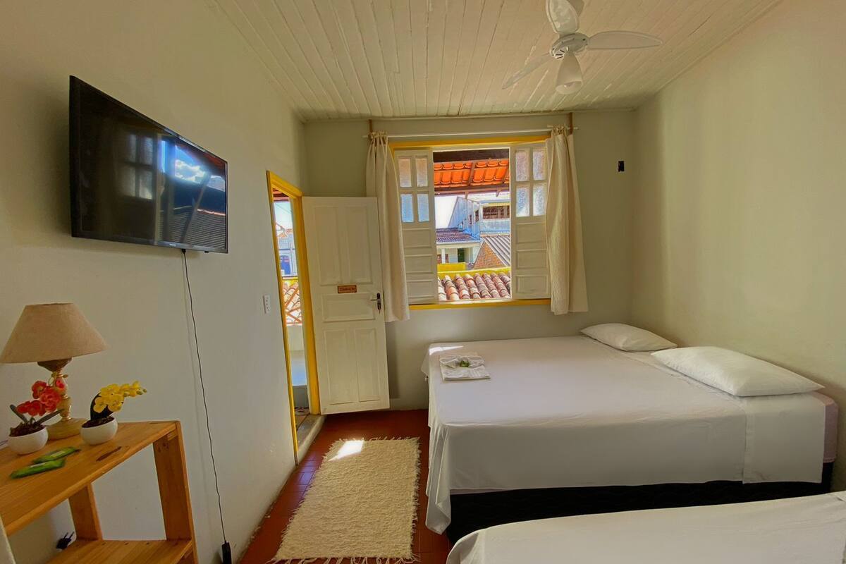 A small, clean room with two beds, a TV, a lamp, and a window with a view of buildings.