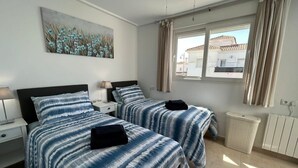 Ein Hotelzimmer mit zwei Betten, einem Bild an der Wand, einem Fenster mit Vorhängen und einer Heizung.