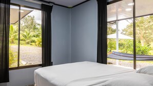 A bedroom with a large bed, two windows with curtains, and a view of a garden. - Uncle Carlos's house (La Tigra)
