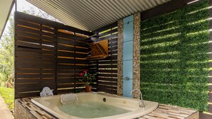 A hot tub with a tiled surround, a wooden slatted roof, and a green wall with foliage. - Uncle Carlos's house (La Tigra)
