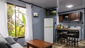 A compact living space with a sofa, a wooden coffee table, a kitchen area with a microwave, stove, and cabinets, and a window with curtains. - Uncle Carlos's house (La Tigra)