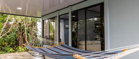 A hammock in a covered outdoor area with a view of greenery and a modern building with large windows.