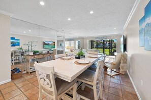 A spacious dining area with a long table set for four, surrounded by white chairs.