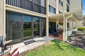 A modern building with large sliding glass doors, a covered patio with outdoor furniture, and a well-maintained lawn.