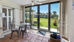 Una habitación con puerta de vidrio que da a un patio, ventilador de techo, una mesa con sillas y una planta en maceta.