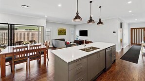 A modern kitchen with a central island, pendant lighting, and a dining area with wooden furniture. - Private Mudjimba Beach Abode (Mudjimba)