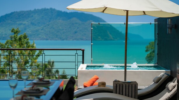 Varanda com vista para uma montanha e área de piscina com espreguiçadeiras e guarda-sol.