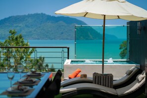 Ein Balkon mit Blick auf einen Berg und einen Poolbereich mit Liegestühlen und Sonnenschirm.