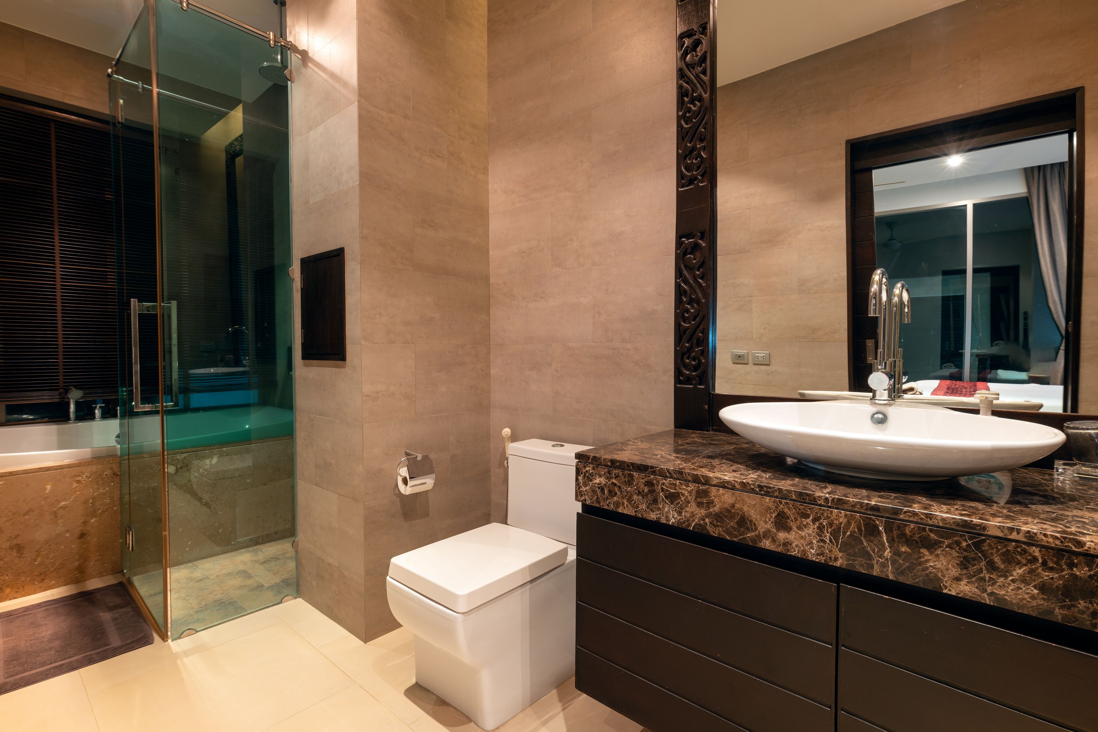 A modern bathroom with a glass-enclosed shower, a white toilet, a large sink, and dark marble countertops.