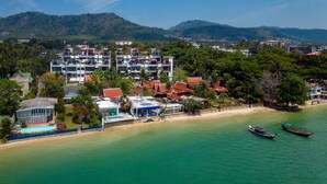 Vista aérea de um hotel à beira-mar, com vários edifícios, uma praia e barcos na água.