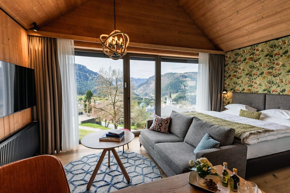 Un dormitorio moderno con una cama grande, un sofá, un televisor y vistas a las montañas.