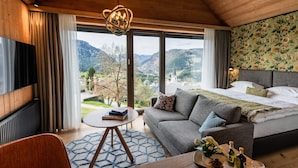 Ein modernes Schlafzimmer mit einem großen Bett, einer Couch, einem Fernseher und Blick auf die Berge.
