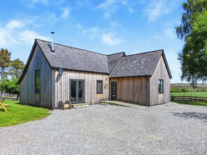 Un bâtiment en bois avec une allée gravillonnée, une porte et une fenêtre.