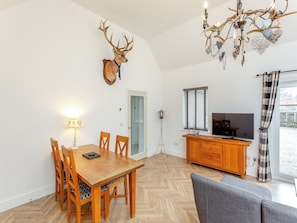 A dining area with a wooden table and chairs, a chandelier, and a mounted deer head on the wall.