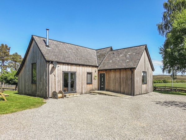 A wooden building with a gravel driveway and a fenced yard.