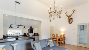 Un soggiorno moderno con un divano a divano grigio, un'area pranzo con sedie in legno, una cucina con piano di lavoro nero e un lampadario con corna di cervo.