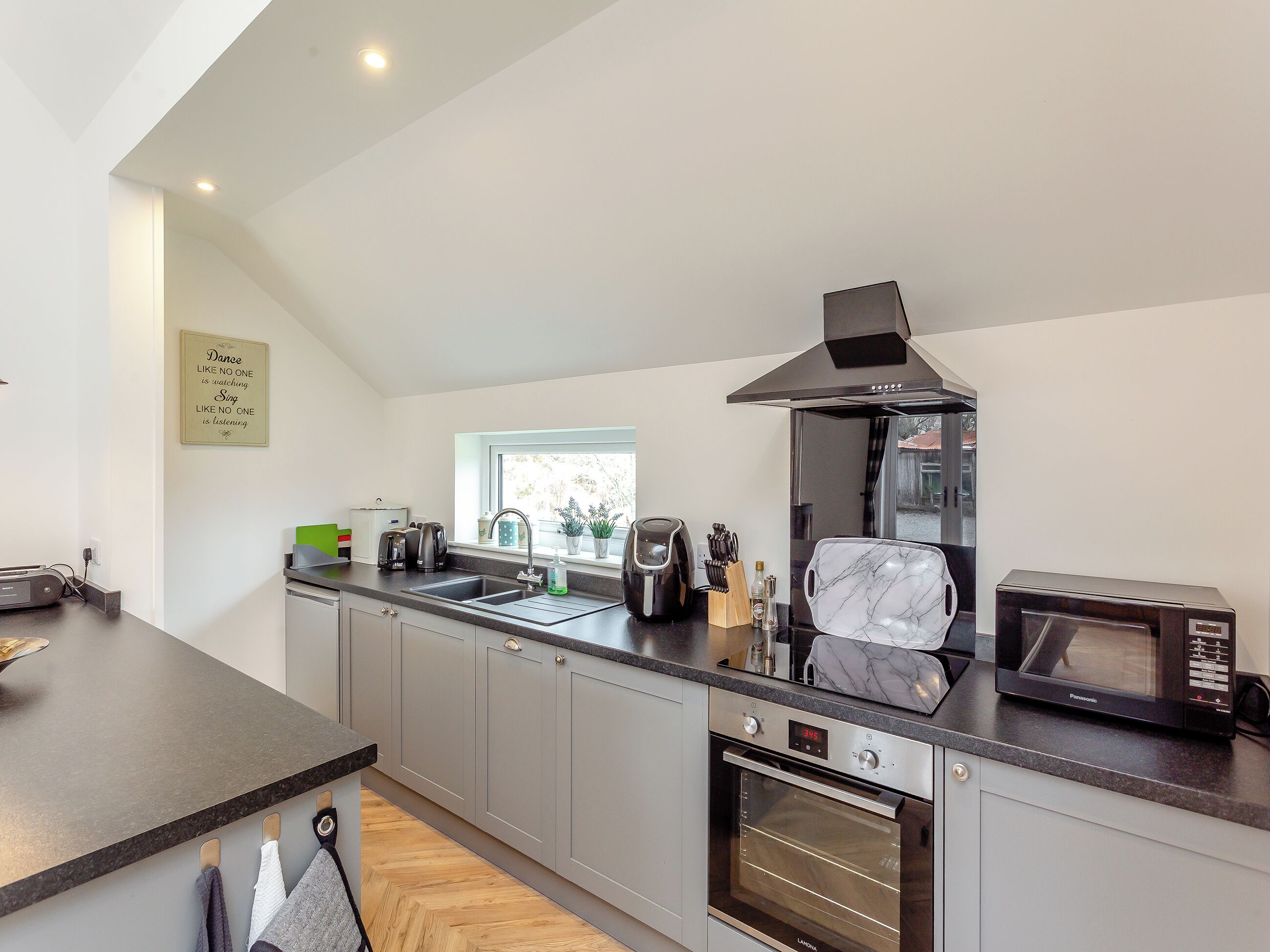 A modern kitchen with grey cabinets, a built-in oven, a microwave, and a window above the sink.