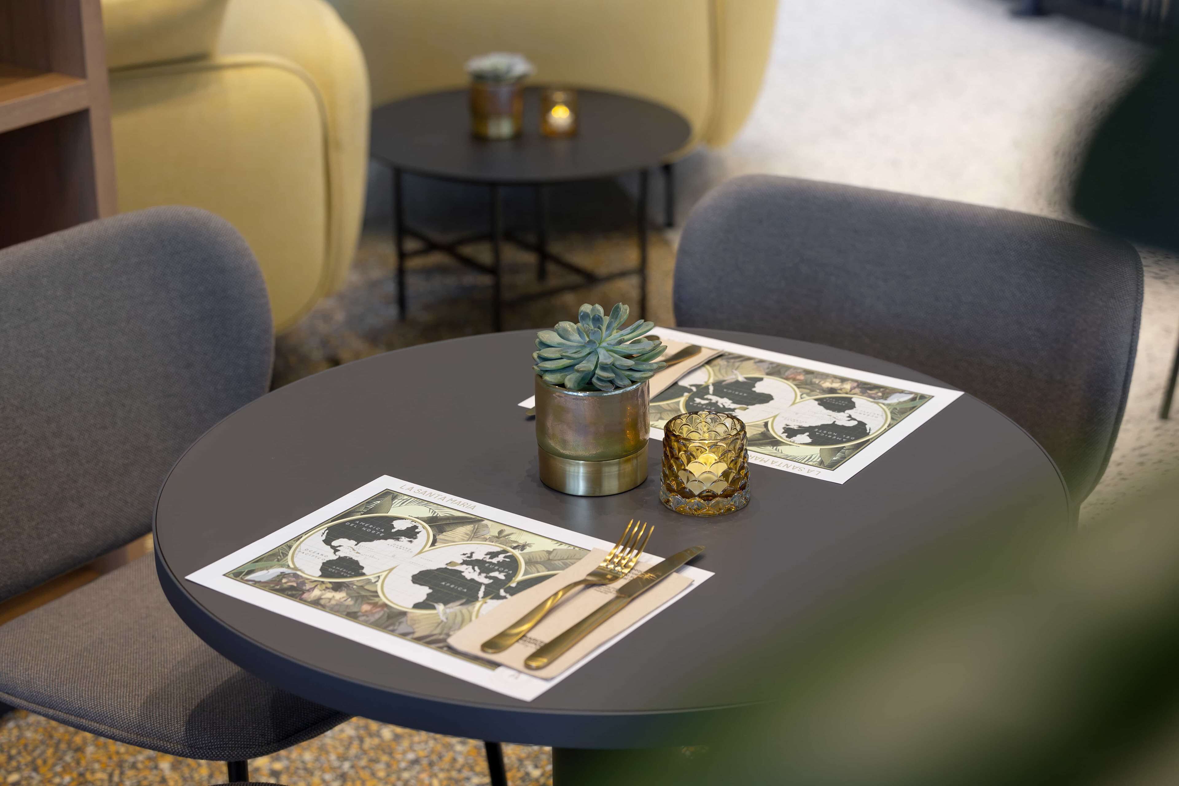 A round table with a placemat, a small potted plant, a candle, and cutlery.