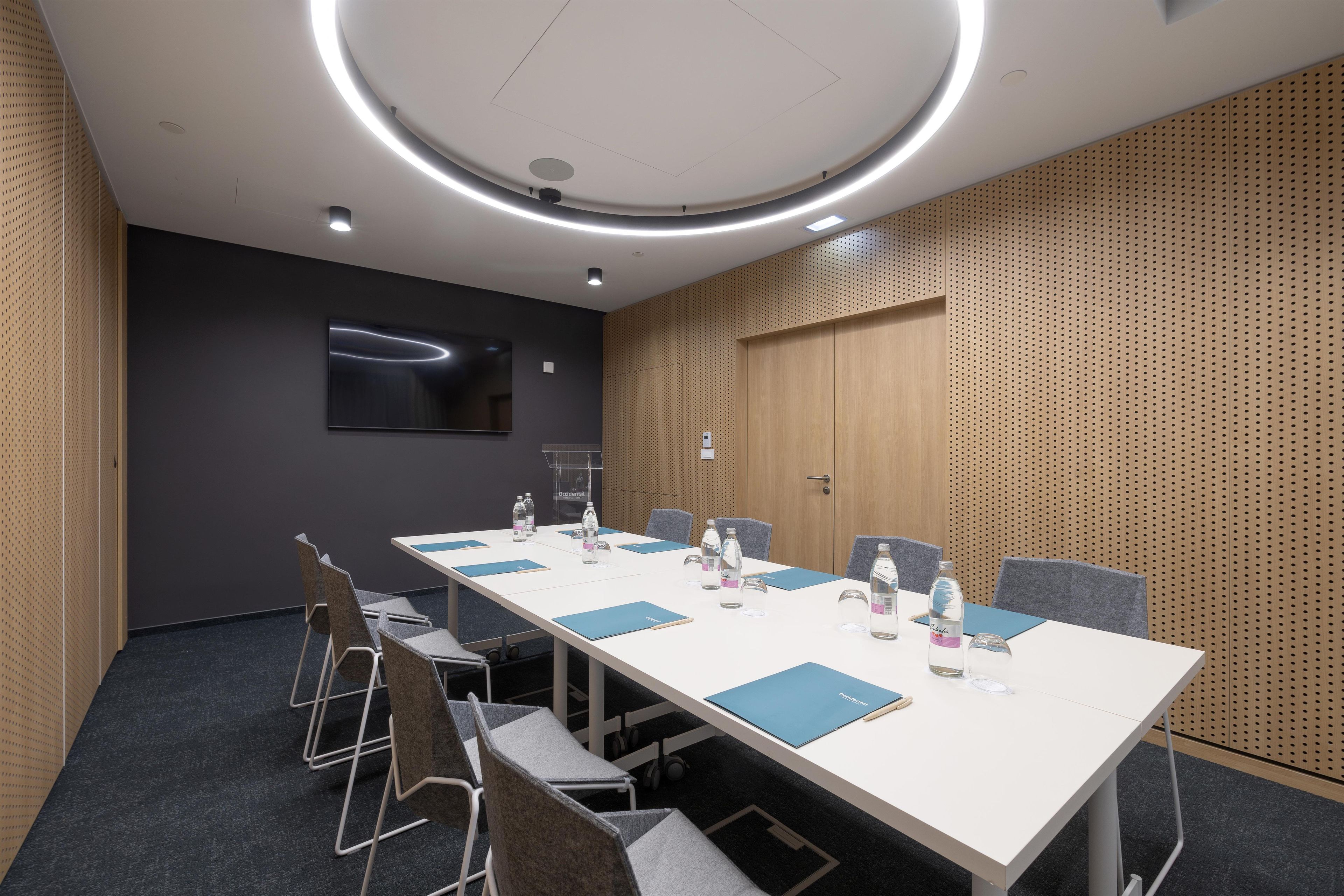 A conference room with a long table, chairs, and a television screen.