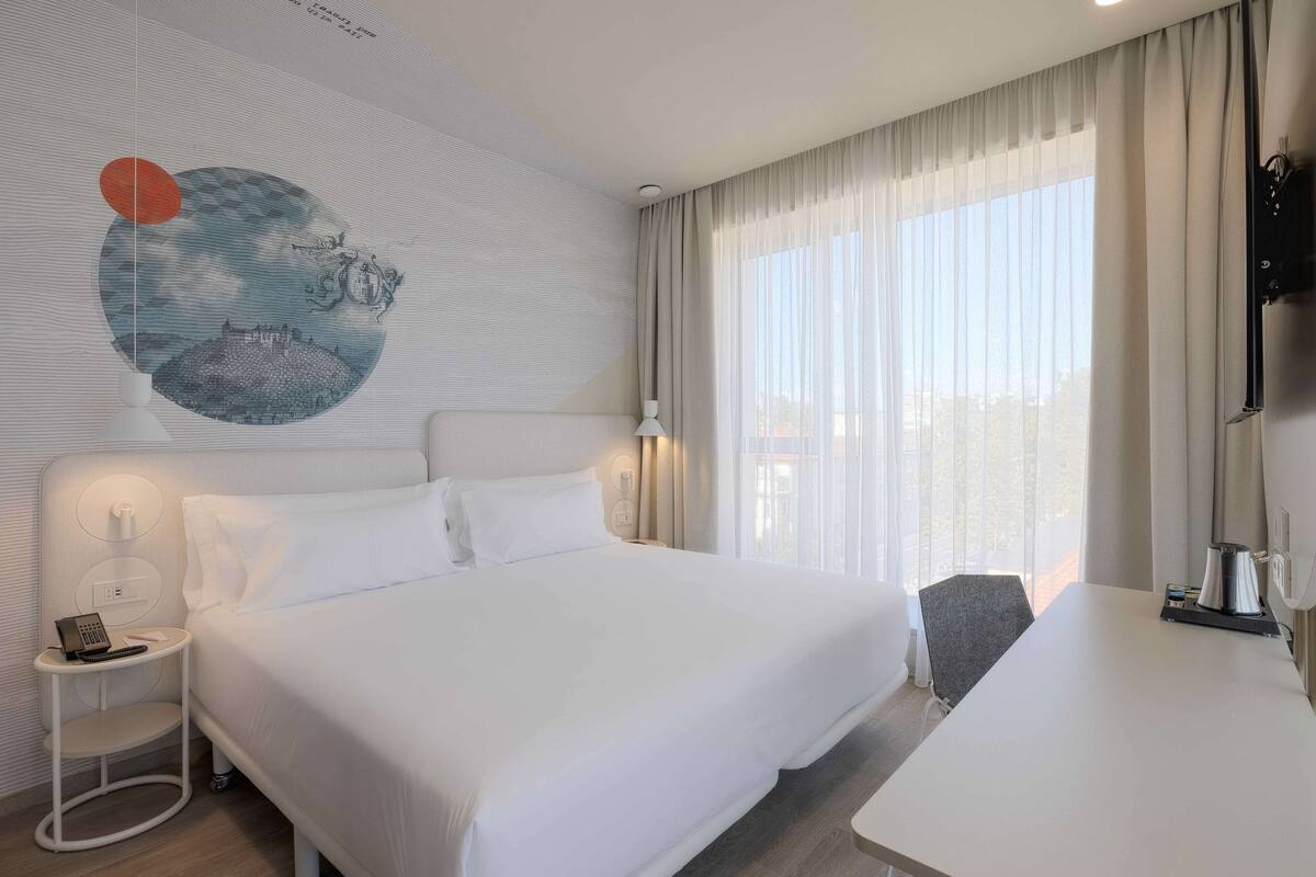 Ein modernes Hotelzimmer mit einem großen Bett, einem Schreibtisch und einem an der Wand befestigten Fernseher.