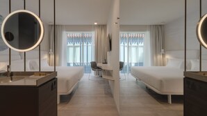 Une chambre d’hôtel moderne équipée de deux lits simples, d’un miroir rond, d’un bureau avec une chaise et d’une grande fenêtre avec des rideaux.