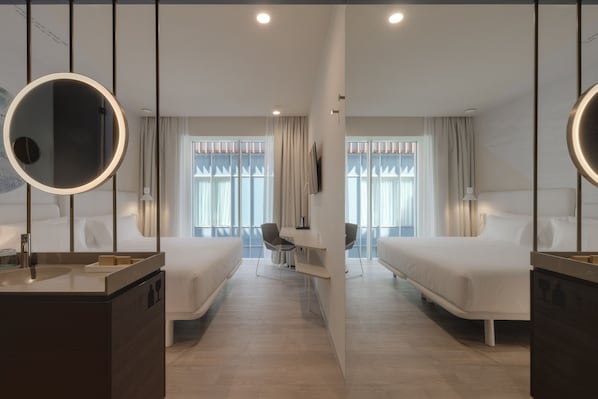 Una habitación de hotel moderna con dos camas individuales, un espejo redondo, un escritorio con una silla y un ventanal con cortinas.