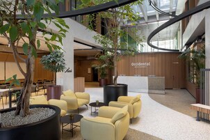 A modern indoor lobby with seating areas, a reception desk, and indoor plants.