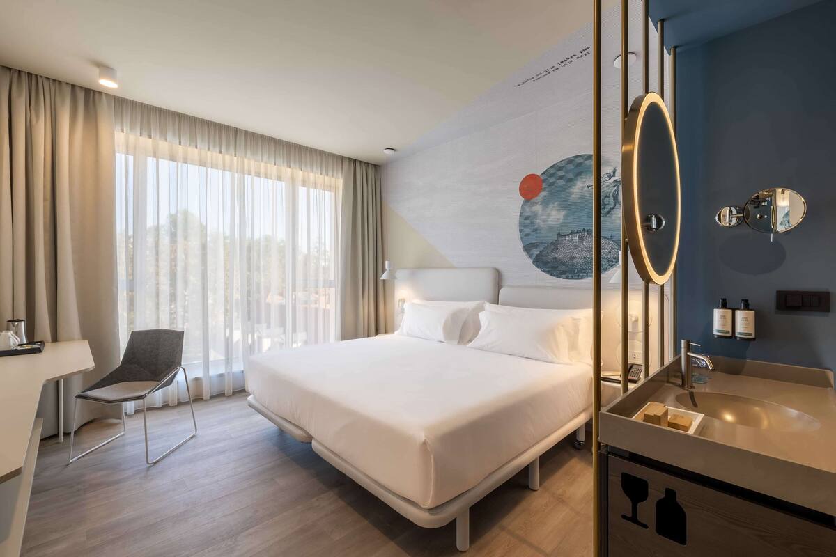 Ein modernes Hotelzimmer mit einem großen Bett, einem Schreibtisch und einem Badezimmer mit Spiegel und Waschbecken.