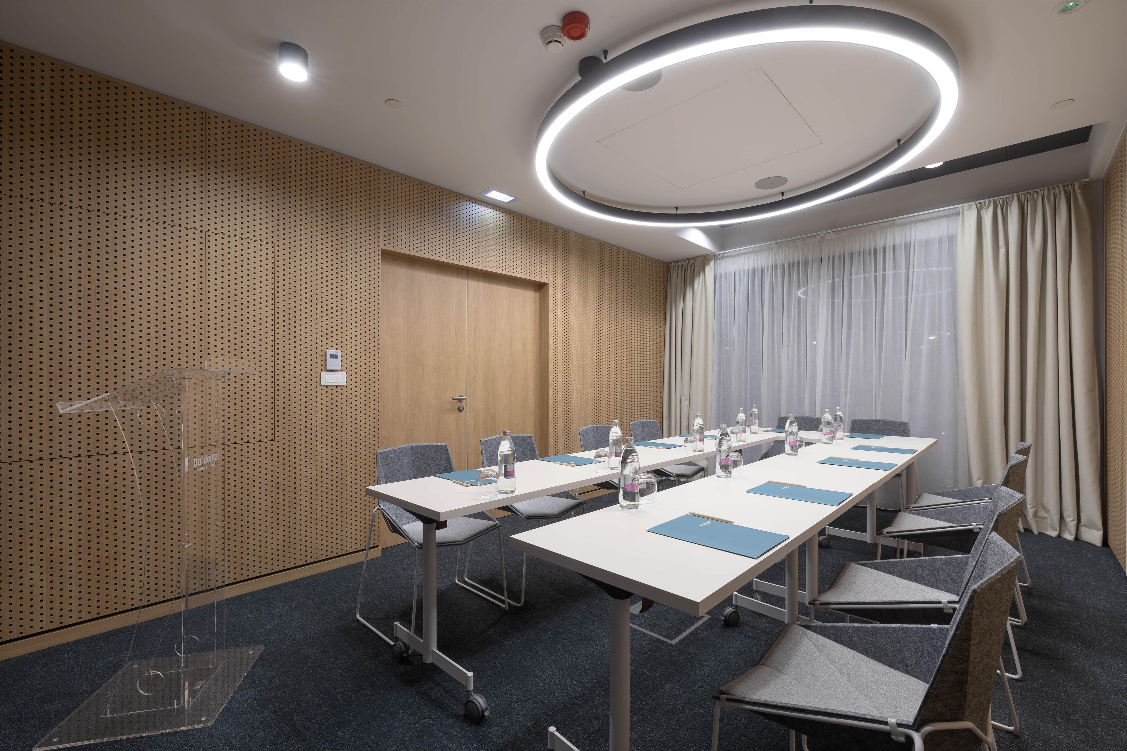 A conference room with a long table, chairs, a podium, and a large window with curtains.
