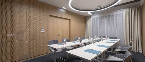 A conference room with a long table, chairs, a podium, and a large window with curtains.