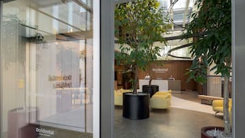 En moderne hotellobby med reception, siddeområde og indendørsplanter.