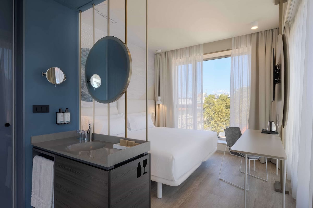 Ein modernes Hotelzimmer mit einem großen Bett, einem Schreibtisch, einem Badezimmer mit großem Spiegel und Blick auf die Stadt.