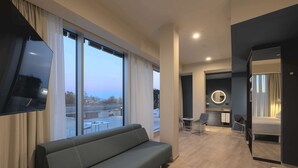 Une chambre d’hôtel moderne équipée d’un canapé, d’un lit, d’une télévision, d’un bureau avec une chaise et d’une salle de bain avec un miroir et des luminaires.
