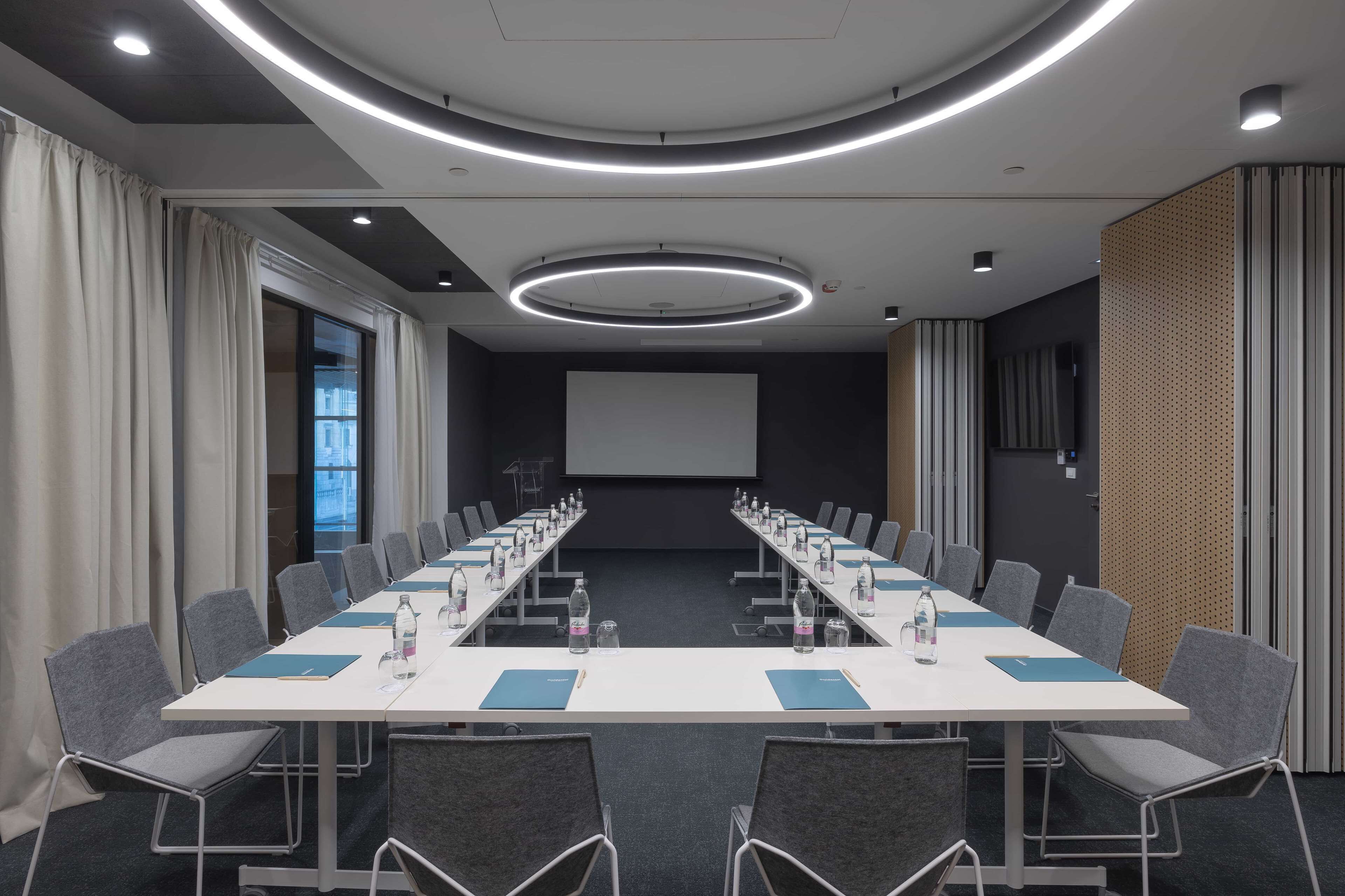 A conference room with a long table, chairs, and a projector screen.