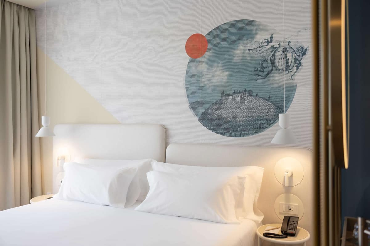 Ein Hotelzimmer mit Bett, weißer Bettwäsche, einem Nachttisch mit Telefon und einem Wandbild in Form eines Kreises.