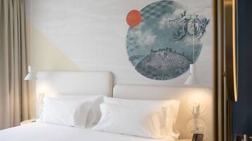 A hotel room with a bed, white bedding, a nightstand with a phone, and a wall with a circular artwork.