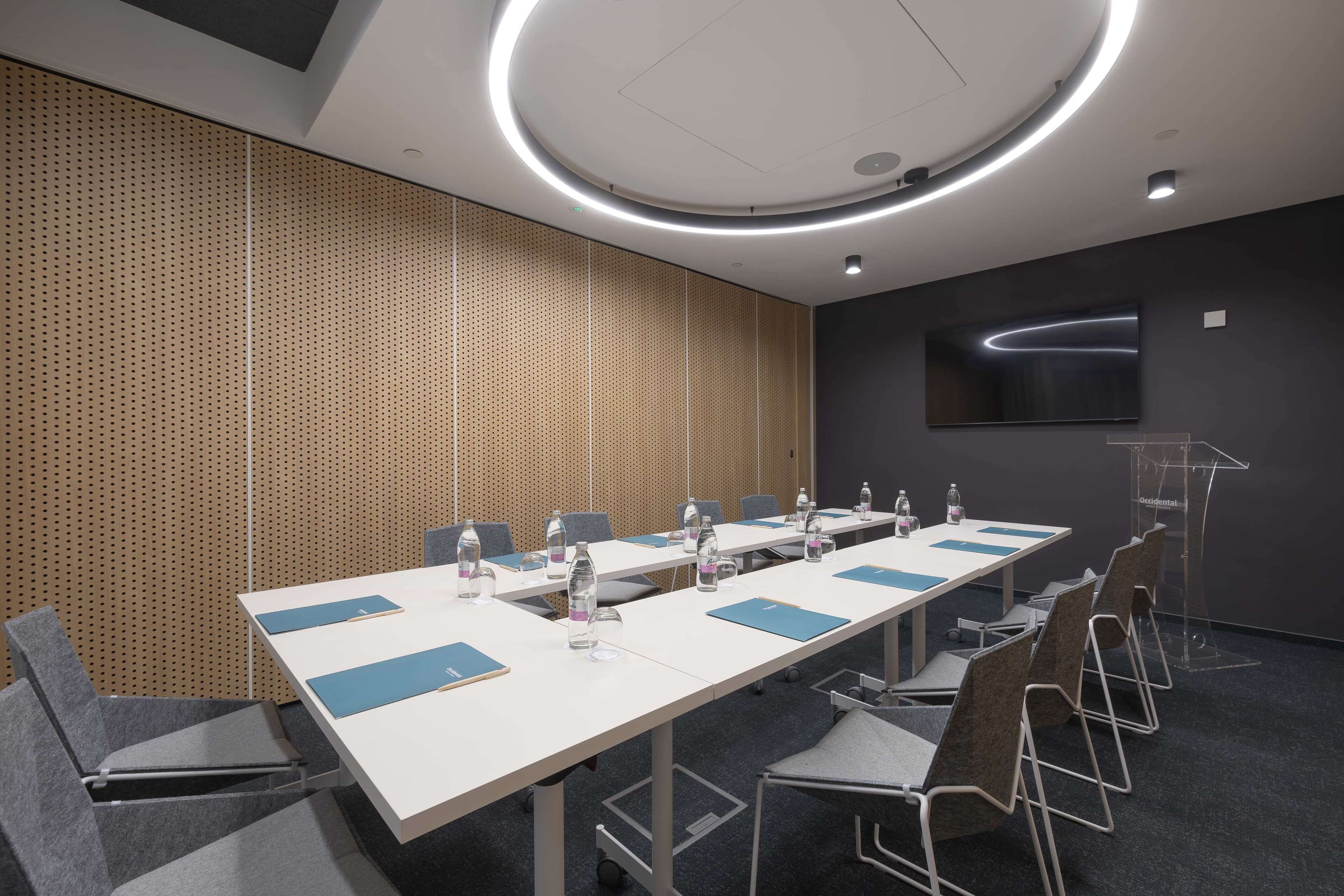 A conference room with a long table, chairs, water bottles, and a podium.