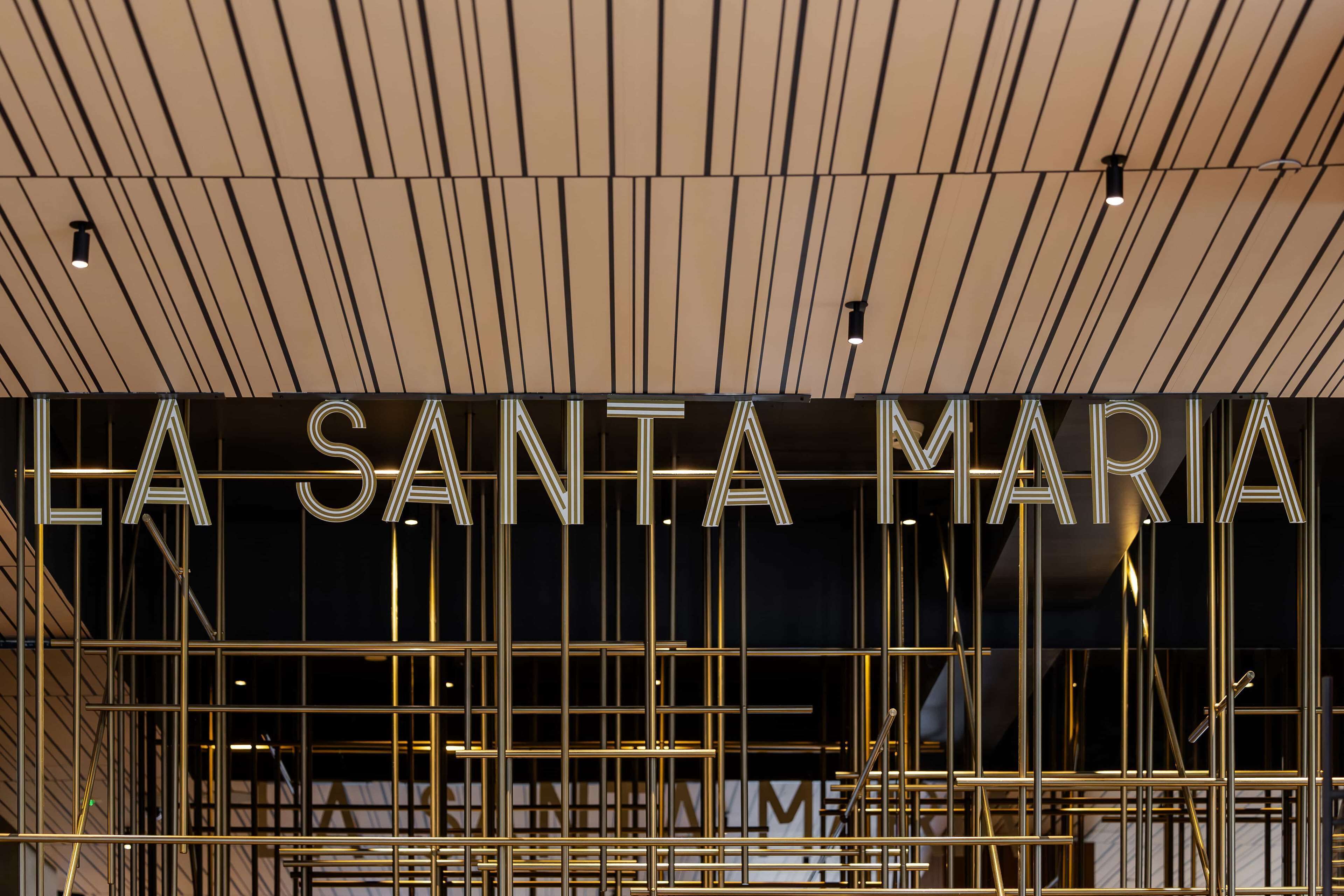 Une entrée d’hôtel moderne, avec le nom « LA SANTA MARIA » affiché en lettres lumineuses, bien en évidence.