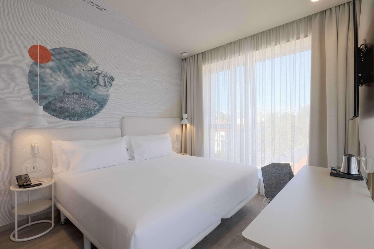 Une chambre d’hôtel avec un grand lit, un bureau, une lampe et un tableau au mur.